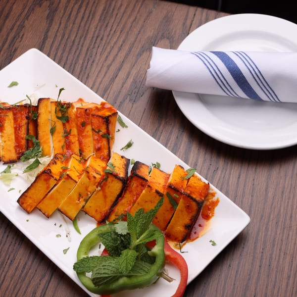 Grilled paneer tikka slices with red sauce and cilantro on a white platter, with a rolled napkin.